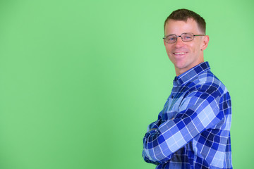 Profile view of happy hipster man smiling and looking at camera with arms crossed