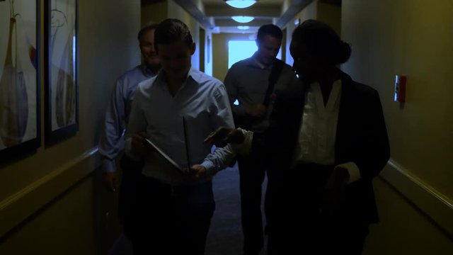 Group Of Business Leaders Walk Down Hotel Hallway Silhouette. Business leaders walk down a dark hotel hallway silhouetted heading to a conference meeting.