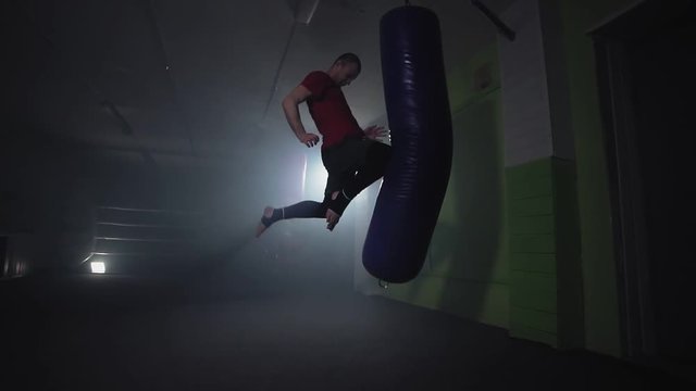 Kickboxer punching in smoky studio. Muay thai fighter training with punching bag on dark background