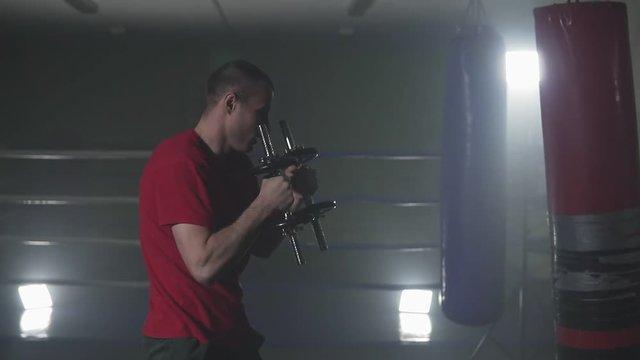Figher training with dumbbells in smoky studio. Kickboxer training punches in low light gym in slow motion. Silhouette on dark background. Weight in hands