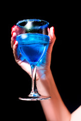 woman holds a glass with a blue cocktail in hand on a black background