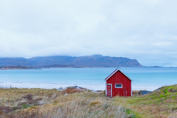 Fototapeta na wymiar Blue water at beach Rambergstranda with typical red fisher hut in Ramberg, Norway
