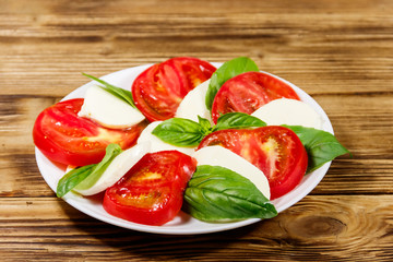 Italian caprese salad with tomatoes, mozzarella cheese and basil on a wooden table
