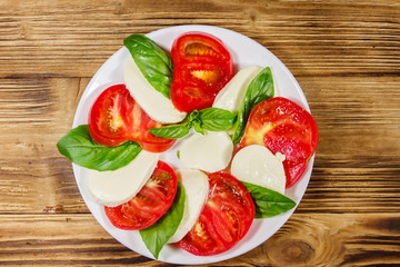 Italian caprese salad with tomatoes, mozzarella cheese and basil on a wooden table. Top view