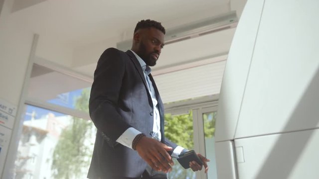 Irritated bank client having problem with ATM credit card got stuck inside the cash machine. Side view of surprised african american man trying to get money in a bank.