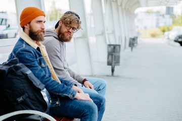 Two srange caucasian bearded men traveler sitting on bench side by side.Travelers waiting at the airport departure area for their delay flight.