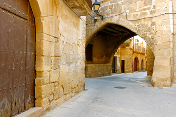 Cozy streets of the Spanish village: a lantern above the arch, old weathered wooden doors, houses with balconies Cretas, Teruel, Aragon, Spain