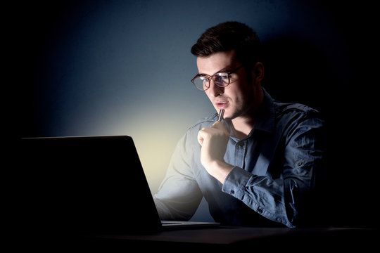 Young handsome businessman working late at night in the office with a dark background