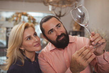 Close up of a mature lovely couple examining wine glass while shopping at homegoods store, copy space. Beautiful woman and her bearded handsome man buying wine glasses together, selective focus