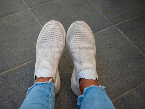 feet of a woman wearing white designer shoes and light blue jeans.