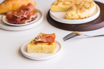  Tortilla,  Spanish omelette made with eggs and potatoes. Traditional Spanish tapa served with slices of jamon, Iberian ham on white background.