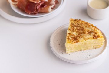  Tortilla,  Spanish omelette made with eggs and potatoes. Traditional Spanish tapa served with slices of jamon, Iberian ham on white background.
