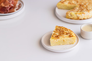  Tortilla,  Spanish omelette made with eggs and potatoes. Traditional Spanish tapa served with slices of jamon, Iberian ham on white background.