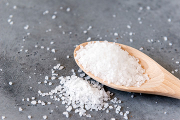 Fototapeta na wymiar large white edible salt on wooden spoon on grey concrete background
