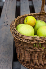 Freshly picked raw organic green yellow apples of various kinds in vintage wicker basket on wood garden table.Autumn fall harvest Thanksgiving abundance concept. Cozy atmosphere. Poster copy space