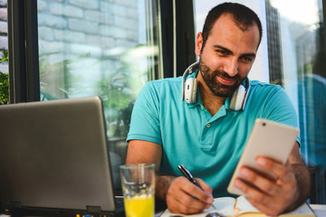 Multi-tasking businessman working in the office. He is using touchpad while reading an e-mail on laptop and taking notes on the paper. Portrait