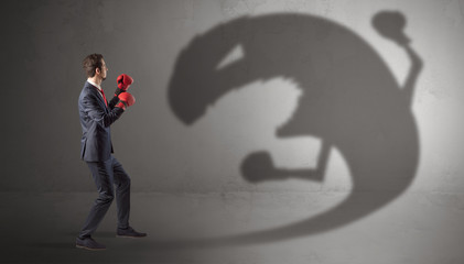 Businessman with boxing glove fighting with a big monster shadow
