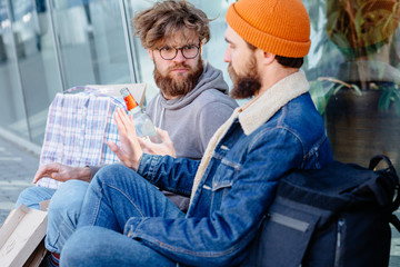Fototapeta premium Inadequate drunk homeless man offering drink for beard hansome guy. Beard man with disgust emotion hand reject glass bottle with offered by homeless person outdoor in city shopping mall on background.