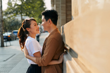 Rear view of a young couple hugging in a destination city while standing in the shopping district near a luxury quality shoe store, outdoors