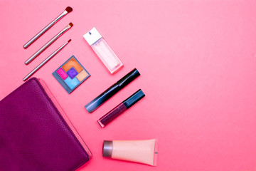 Makeup products, color pallette and different sizes of brushes with cosmetic bag in pink background