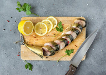 sliced smoked mackerel with spices and lemon on a chopping Board  on a grey background, top view,