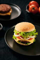 Hamburger with beef meat burger and fresh vegetables on dark background. Tasty fast food