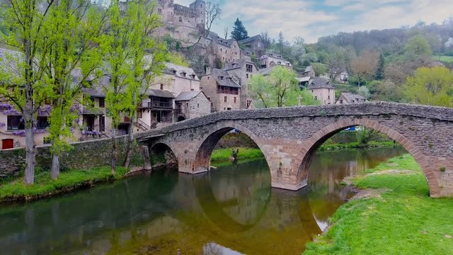 Flight crossing Aveyron river and old stone bridge on the medieval village of Belcastel, Aveyron, France.