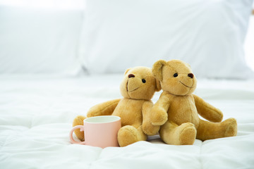 Two Teddy Bear lying in the bed with pink cup of coffee