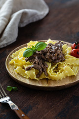 Beef stroganoff in a wooden plate on a dark rustic wooden background.