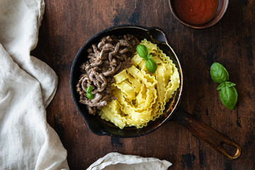 Beef stroganoff in a frying pan on a dark rustic wooden background.