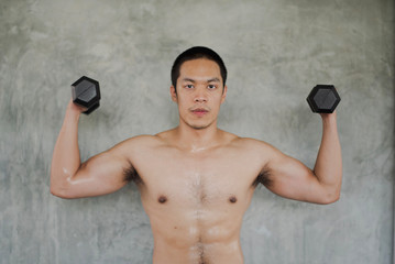 Young Asian man exercising with dumbbells and looking at the camera in the gym. man workout at fitness room. man losing weight training.
