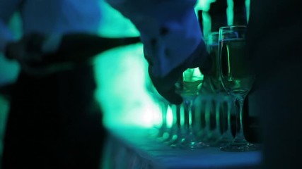 The waiter pours champagne into glasses at the celebration. People at a festive event take glasses of champagne from the table. Color lights party. Subdued light, night club atmosphere