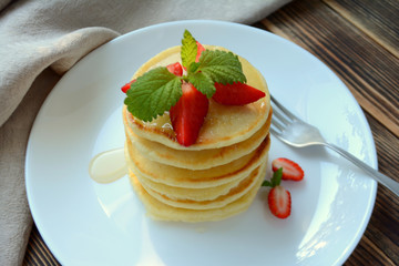 Stack of pancake with strawberries, honey and mint on a white plate