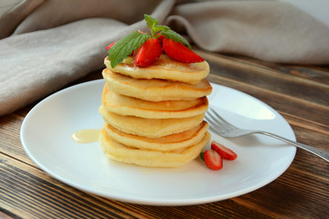 Stack of pancake with strawberries, honey and mint on a white plate