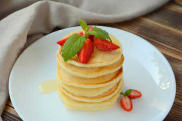 Stack of pancake with strawberries, honey and mint on a white plate