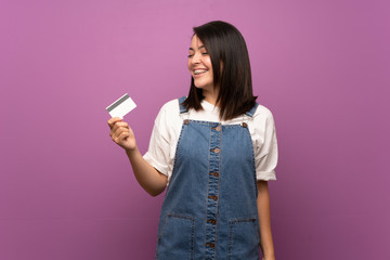 Young Mexican woman over isolated background holding a credit card