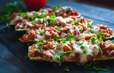 Close-up of stuffed zucchini boats with ground beef, spicy tomato sauce, cheese and fresh parsley, on dark background