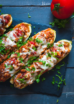 Close-up of stuffed zucchini boats with ground beef, spicy tomato sauce, cheese and fresh parsley, on dark background, top view
