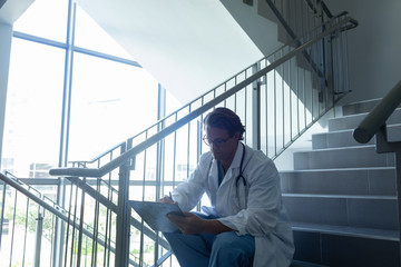 Male surgeon writing on clipboard while sitting on stairs at hospital