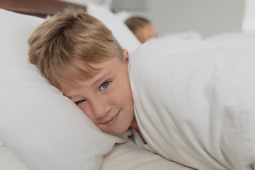 Cute boy looking at camera while lying on bed in bedroom at comfortable home