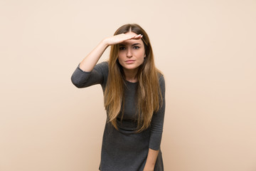 Young woman over isolated background looking far away with hand to look something