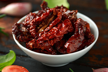 Sun dried tomatoes in white bowl with fresh herbs and spices on wooden table