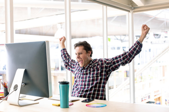 Male graphic designer celebrating success at desk in a modern office