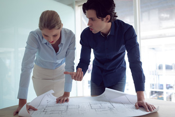 Male and female architects discussing over blueprint in office