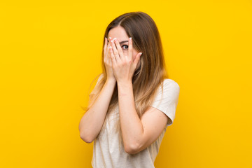 Young woman over isolated yellow wall covering eyes and looking through fingers