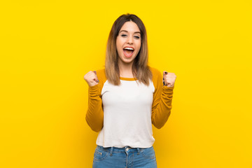 Pretty young woman over isolated yellow wall celebrating a victory in winner position