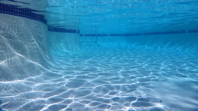 Empty underwater swimming pool with moving patterns of sunlight.