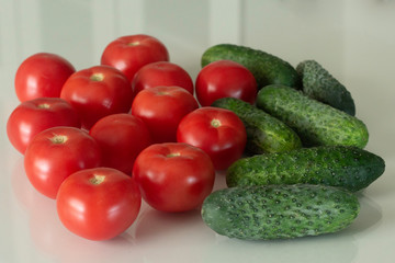 Fresh tomatoes and cucumber on a white glass kitchen table. Fresh organic food ingredients. Top view.