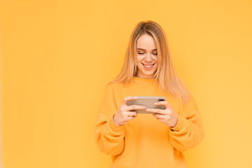 Portrait of a smiling girl in bright orange clothes is with a smartphone in her hands on a yellow...