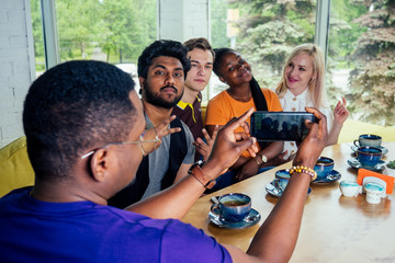 multinational group of happy friends enjoy and drinking tea and taking photos selfie on photocamera in cafe .